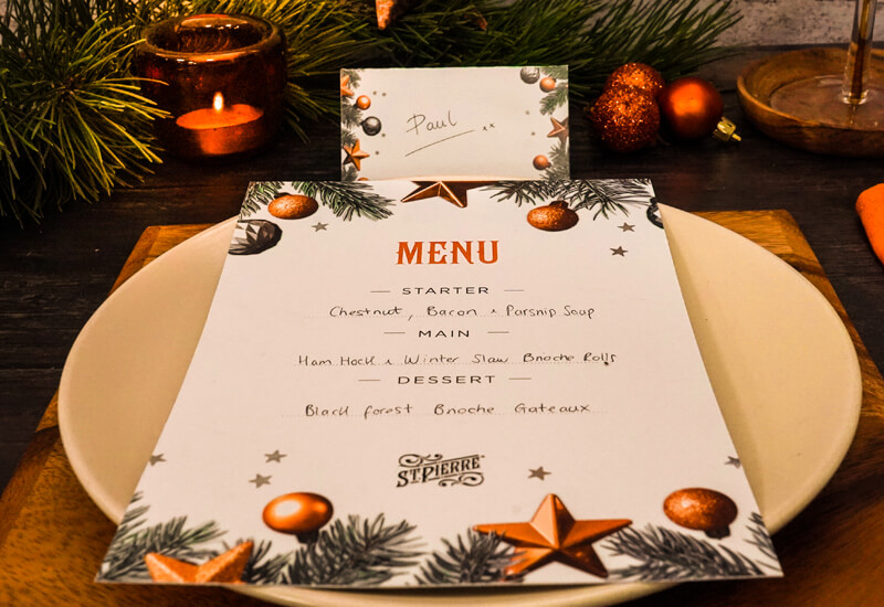 A close up of a Christmas themed menu card on a plate with Christmas decorations in the background
