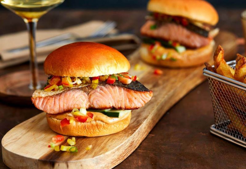 blackenedsalmonburger A photo of two burger buns filled with salmon fillets and diced vegetables, on a wooden board