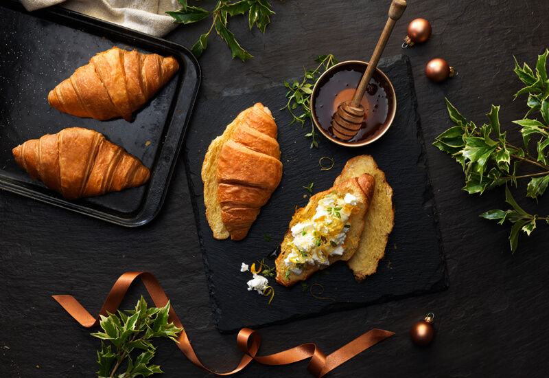 An overhead photo of croissants on a slate mat with goats cheese and honey on one of them