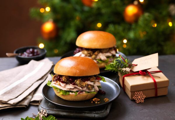 Two turkey, stuffing and cranberry burgers on plates in front of a Christmas tree with a Christmas present next to them