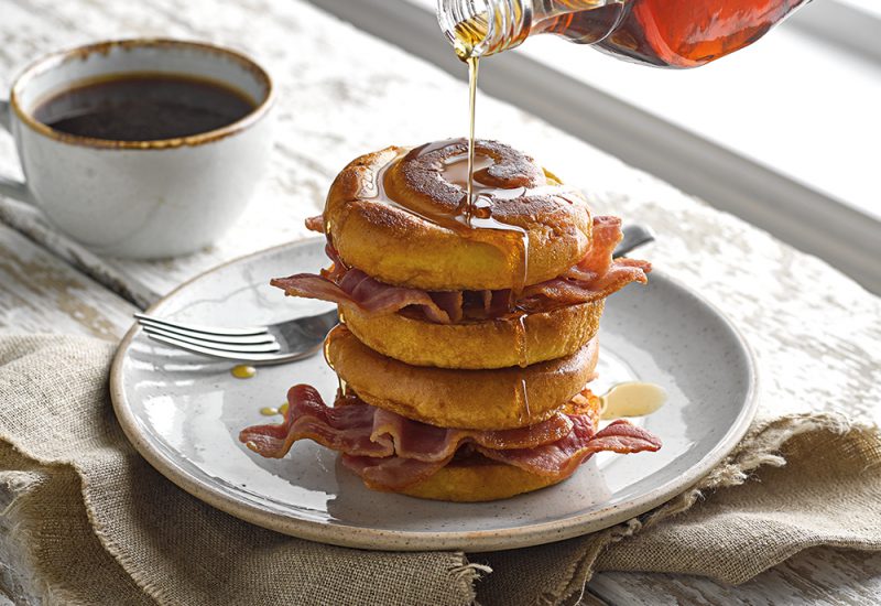 sp_web__0005_french_toast_swirl_cmyk_small A stack of St Pierre Brioche Swirls on a plate with fried bacon in between them, and covered in maple syrup