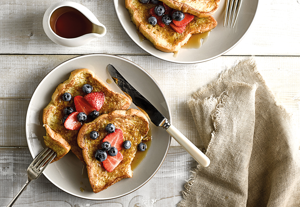 An overhead photo of a Brioche French Toast recipe on a plate with cutlery, napkin and syrup