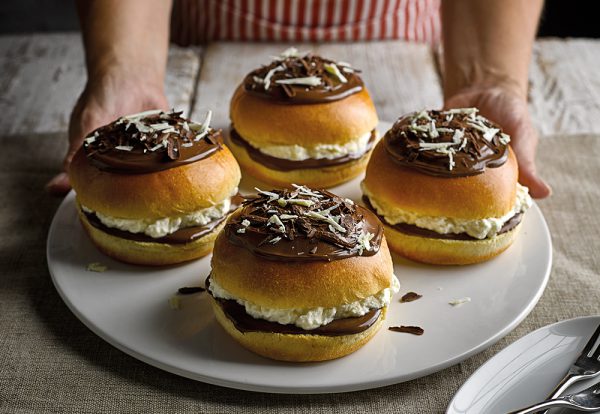Four St Pierre Brioche Burger Buns filled with whipped cream and melted chocolate, and topped with chocolate, on a white plate