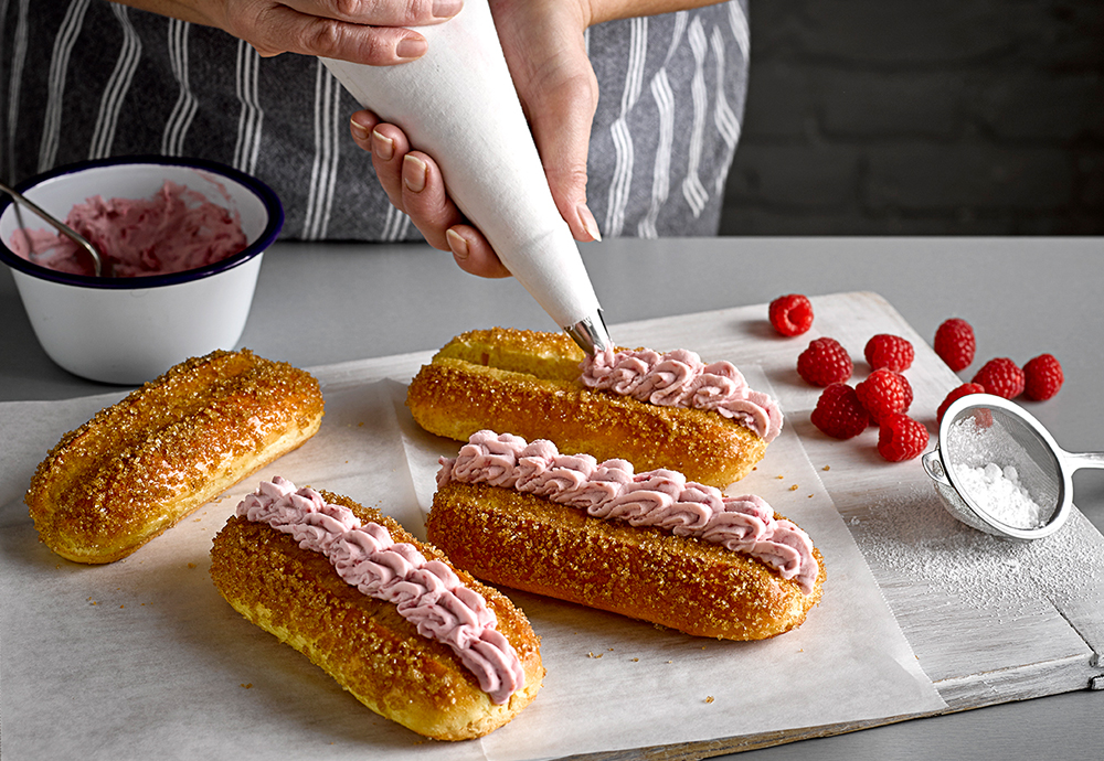 sp_web_productshots_2_0003_ukraspberrymascarponerollsre Four St Pierre Brioche Hot Dog Rolls being filled with a raspberry cream from a piping bag held by a woman