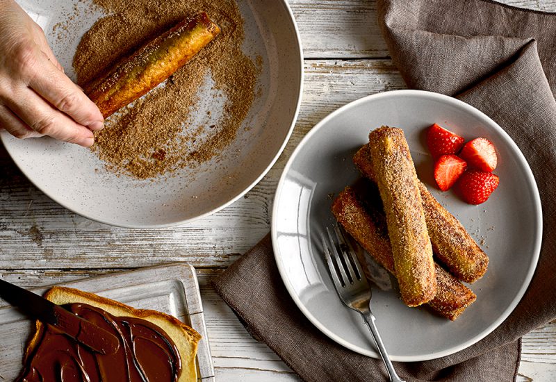 sp_web_productshots_2_0005_uknuttelarollsupsre Slices of brioche loaf rolled up and dusted in a cinnamon sugar on two plates with chopped strawberries