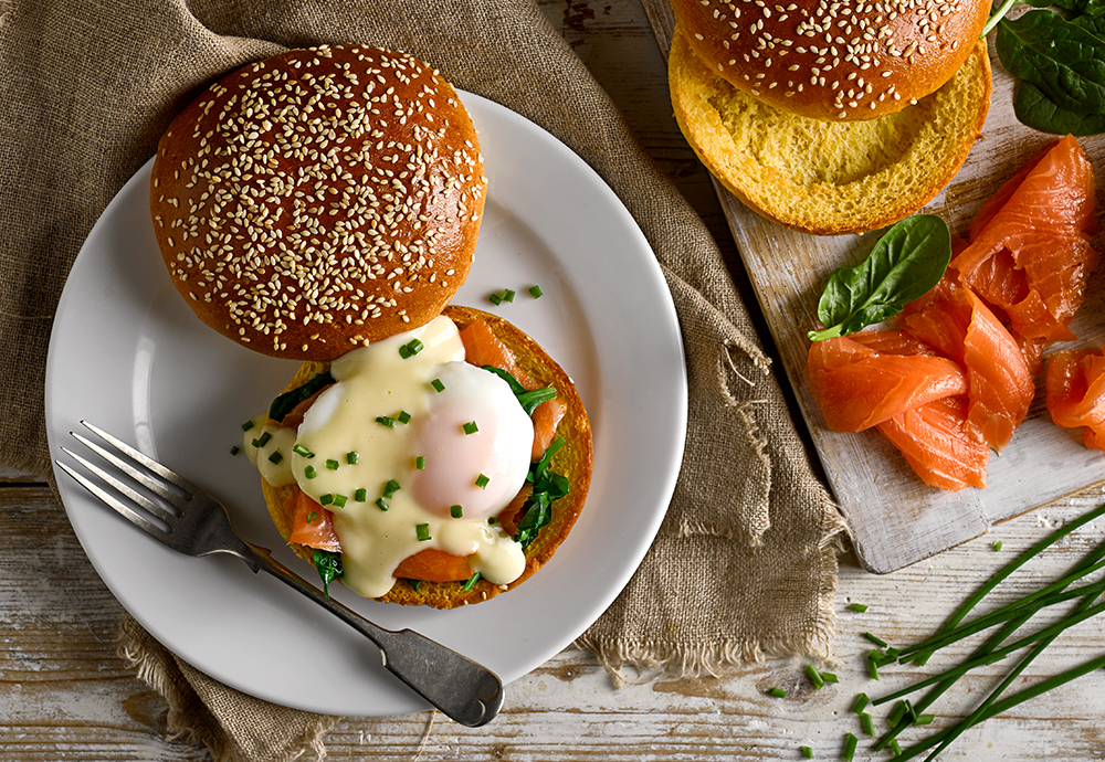 A poached egg, smoked salmon and lettuce leaves on a seeded brioche burger bun on a plate with a forkburger - Breakfast Brioche