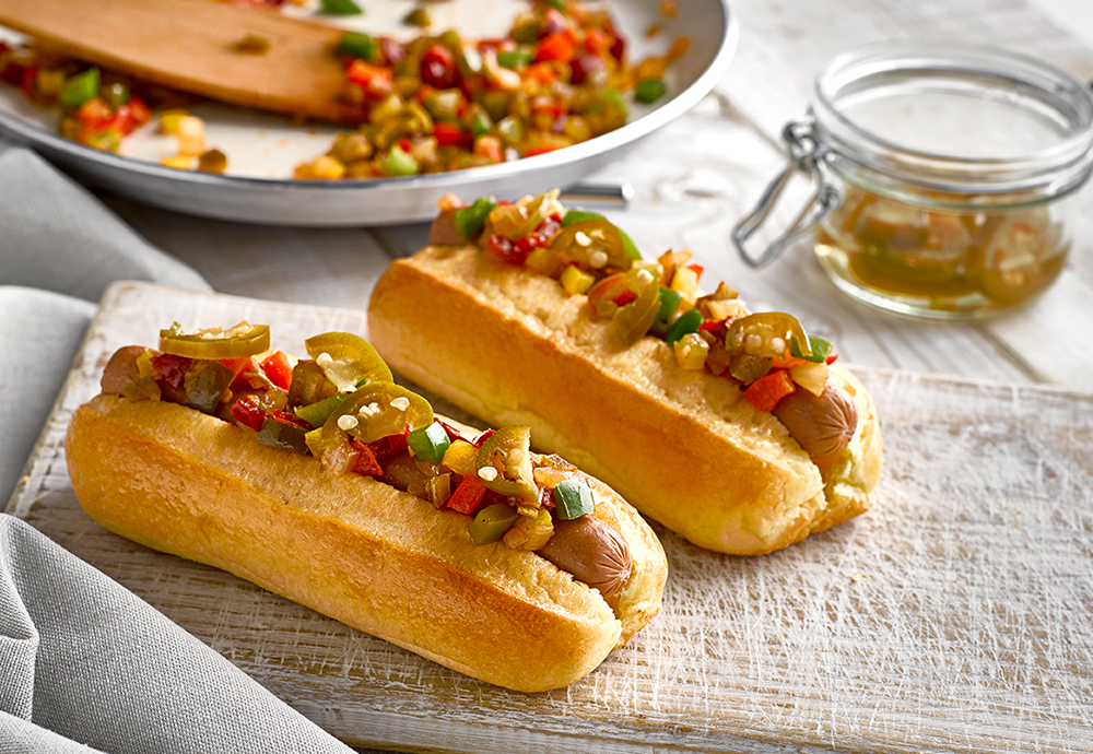sp_web_productshots_2_0012_ukchillidogre Two St Pierre Brioche Hot Dog Rolls filled with a sausage, and topped with sliced Jalapeño peppers and diced peppers