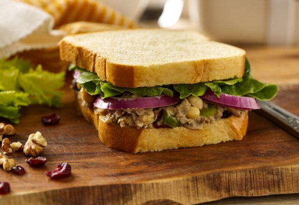 A close up of a sandwich filled with chickpeas, red onion slices and salad leaves on a wooden board