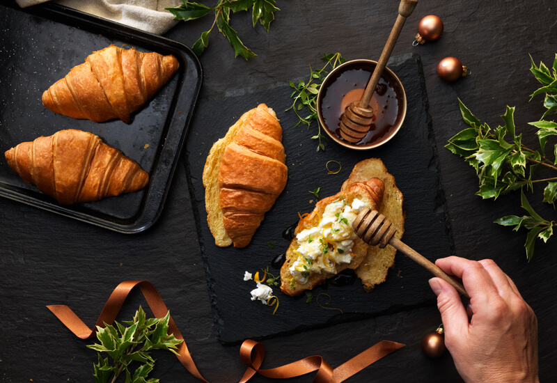 An overhead photo of croissants sliced in half and topped with goats cheese and honey drizzled on top